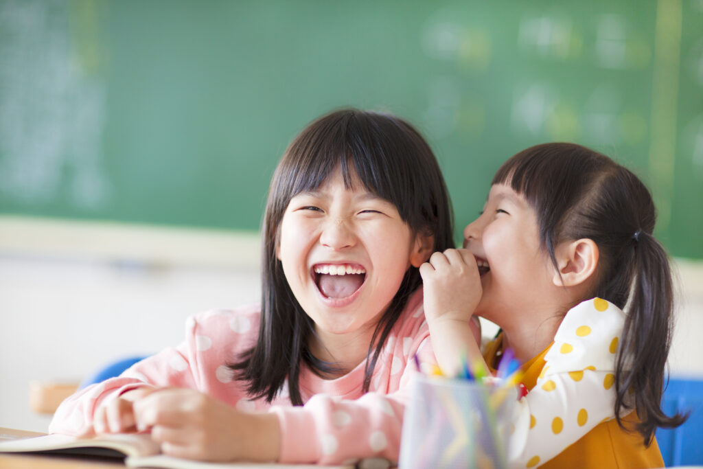 Laughing little girls sharing secrets in class