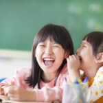 Laughing little girls sharing secrets in class